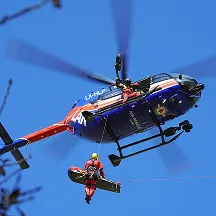 Rescue helicopter in blue sky lifting a person in a red suit with a rescue harness.