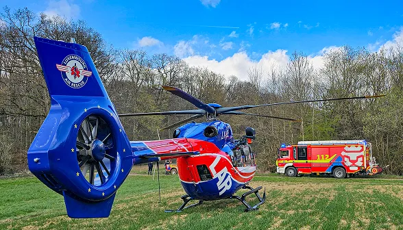 Blue and red emergency medical rescue helicopter on grass field with fire truck in the background under a partly cloudy sky.