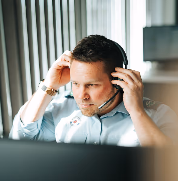 Homme aux cheveux courts portant un casque et une chemise bleu clair, se concentrant tout en travaillant devant un ordinateur.