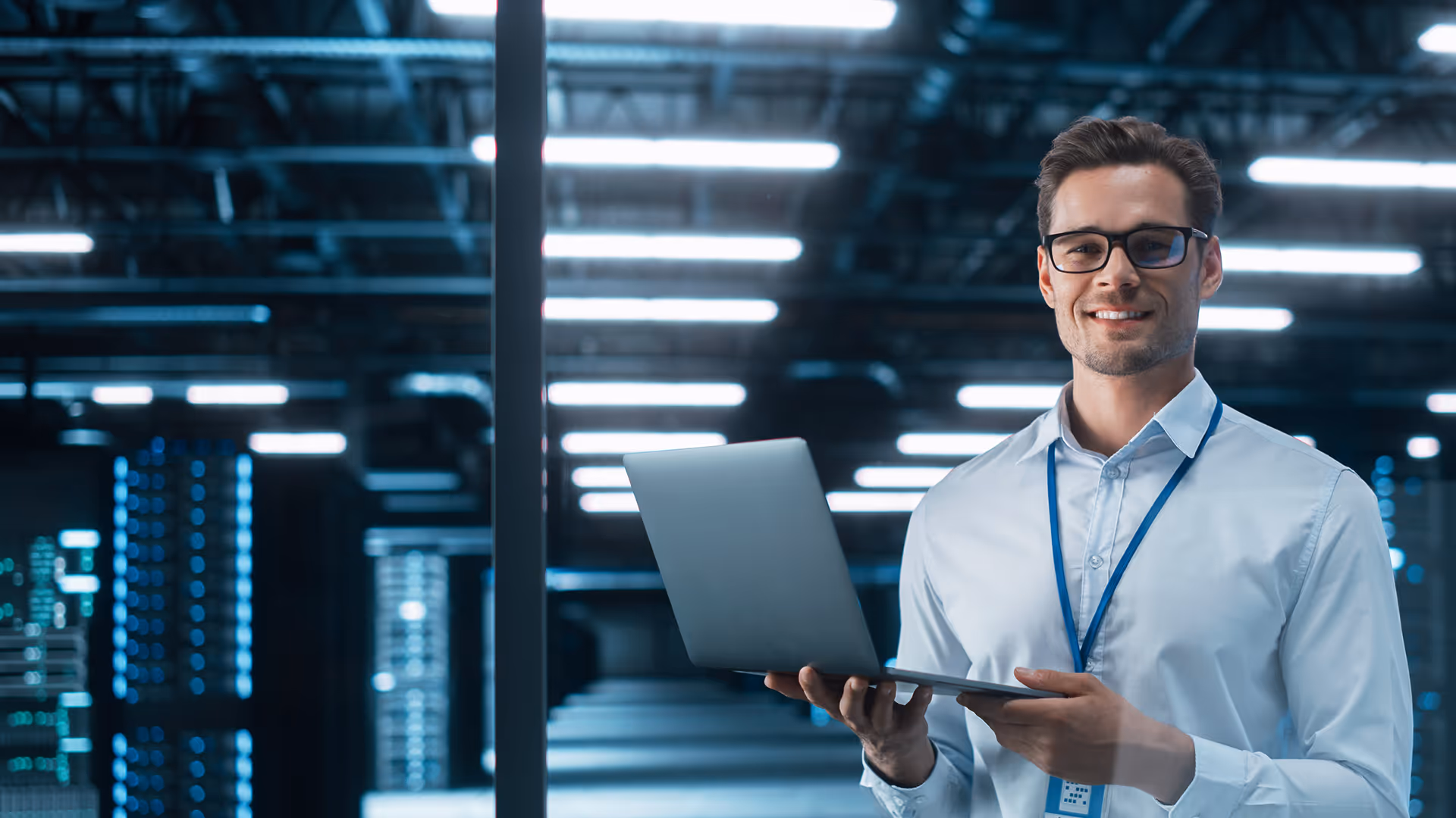 A man stood holding a laptop in front of servers in a data center