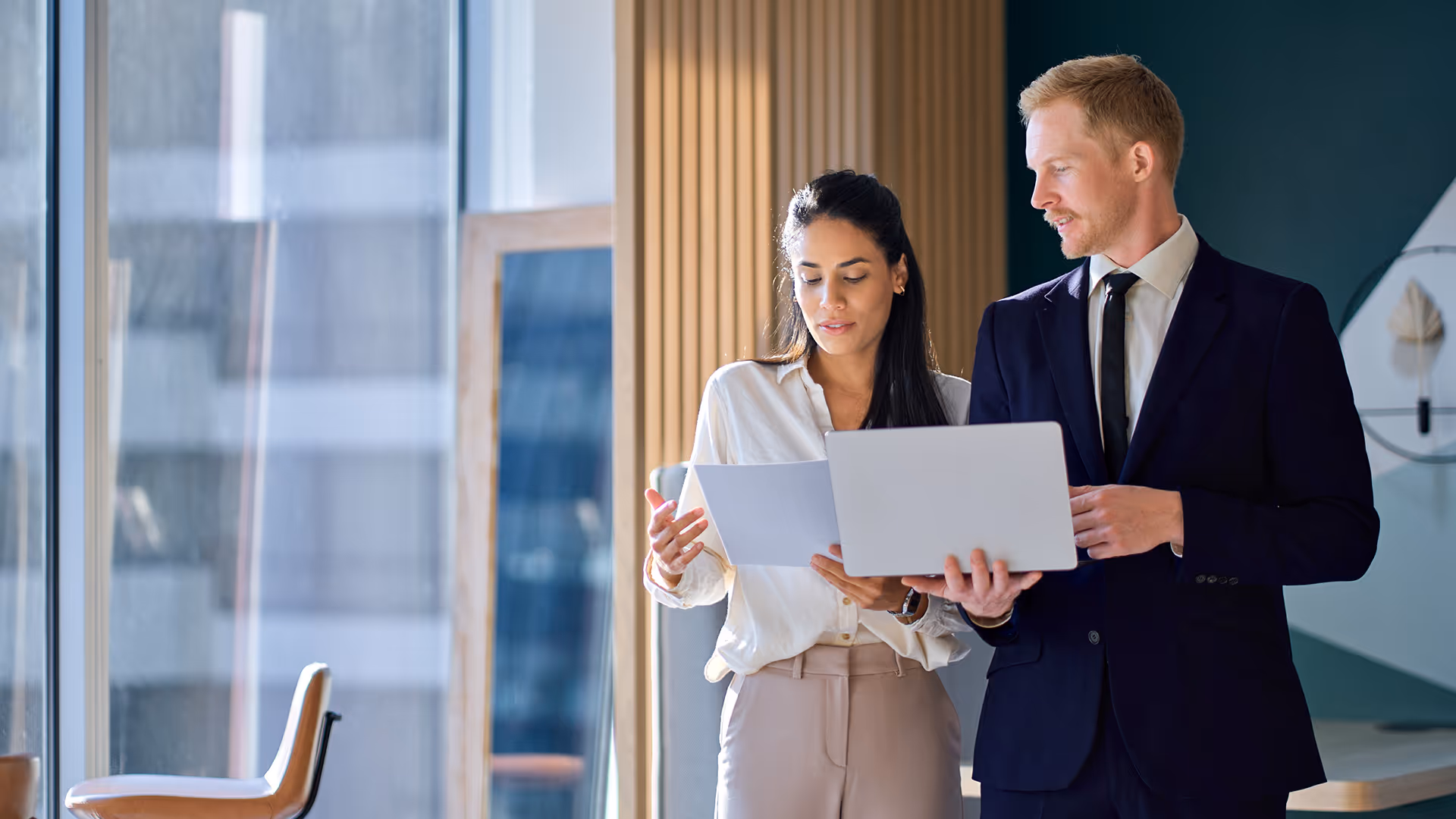 Two people looking at insurance information on a laptop and document — representing card issuing settlement cover