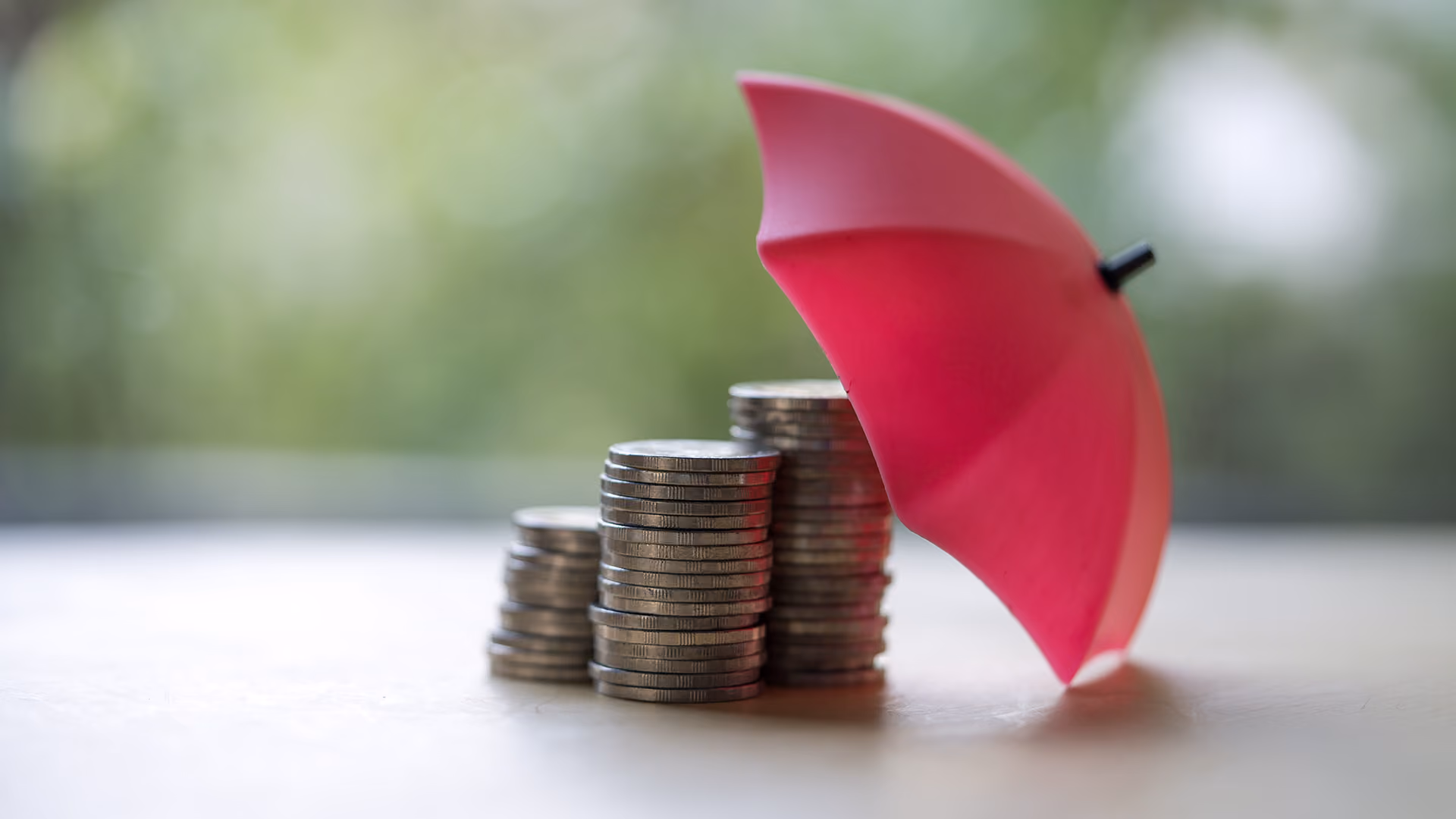 Stack of coins beneath an umbrella, representing protected finances