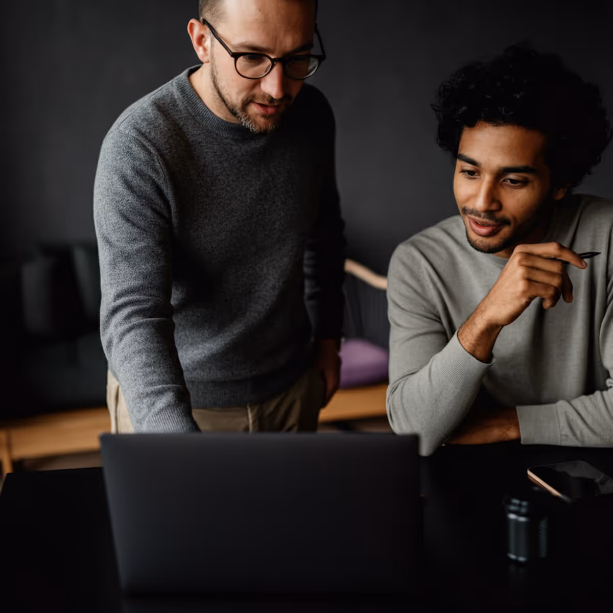Two men collaborating while looking at a laptop in a modern workspace.