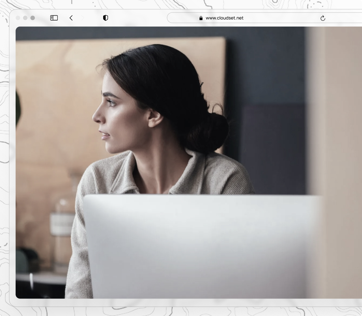Woman with dark hair in a bun looking to her left behind a laptop in a softly lit workspace.
