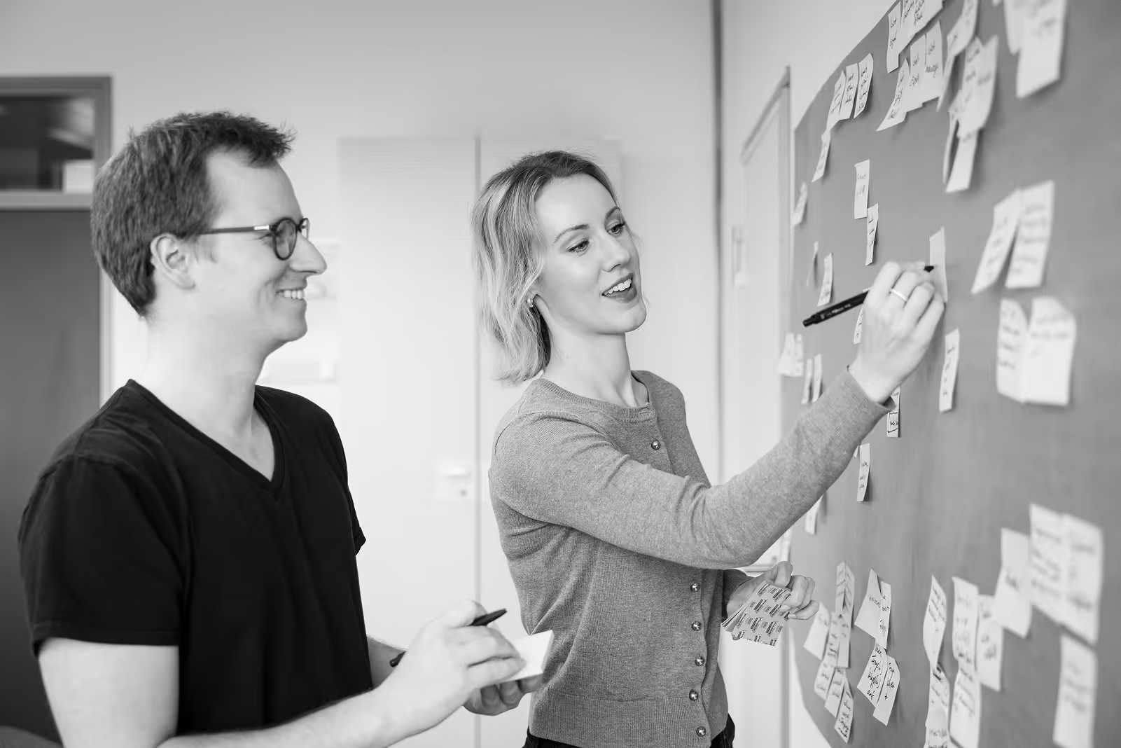 Zwei Teammitglieder diskutieren gemeinsam vor einer Pinnwand mit Post-its.