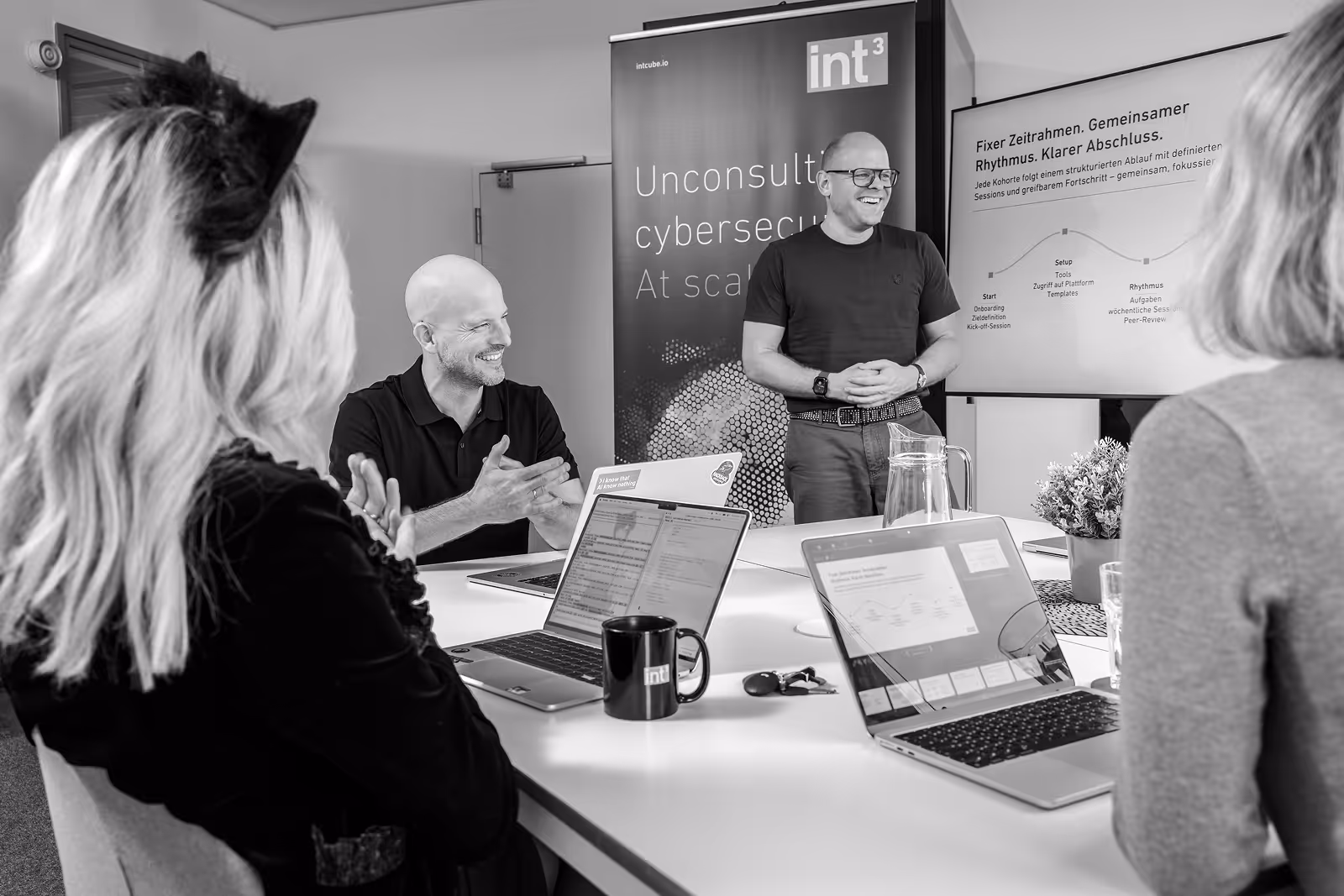 Vier Mitarbeitende im Workshop mit Laptops, eine Person präsentiert an Leinwand.