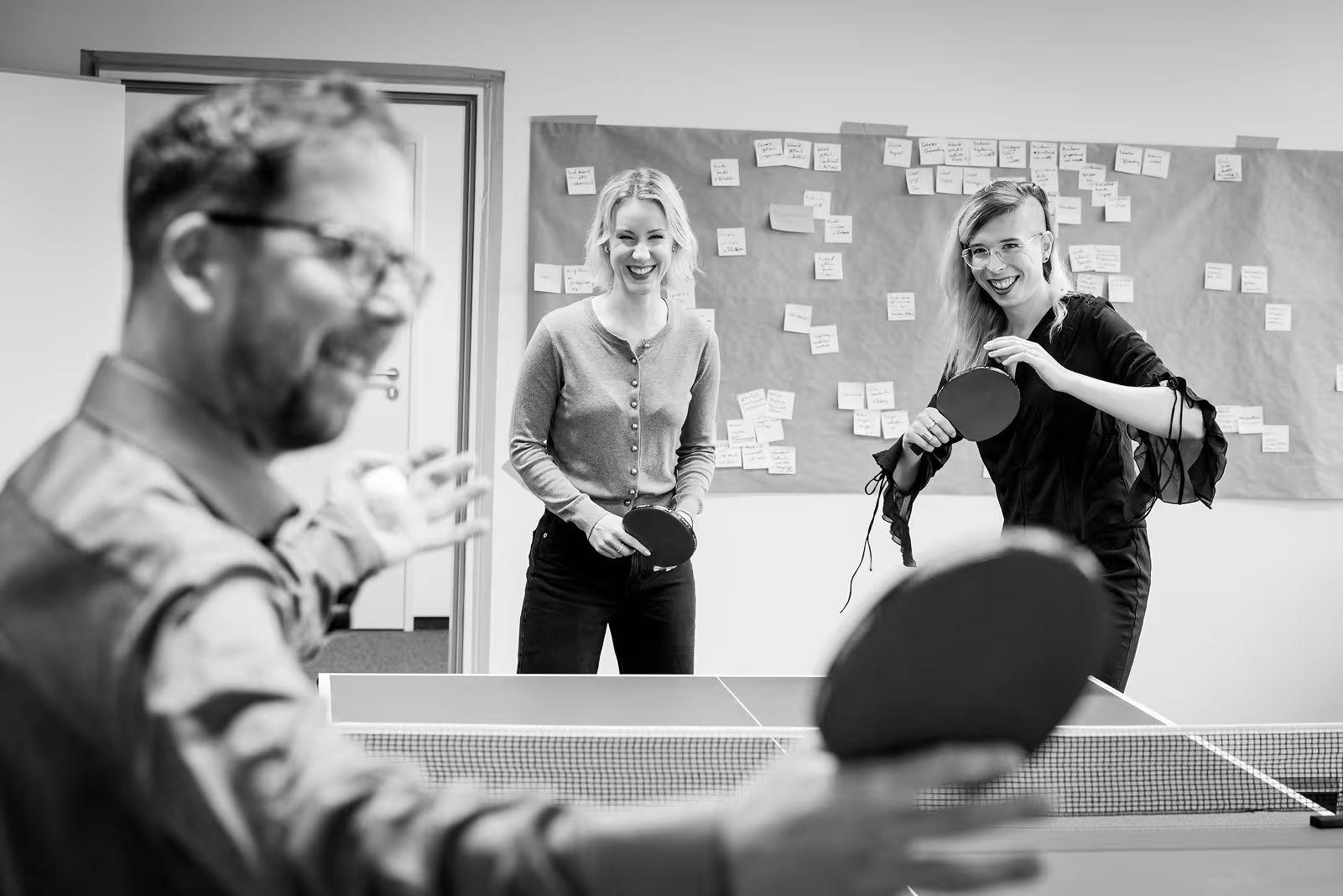 Tischtennis im Büro mit drei lachenden Mitarbeitenden.