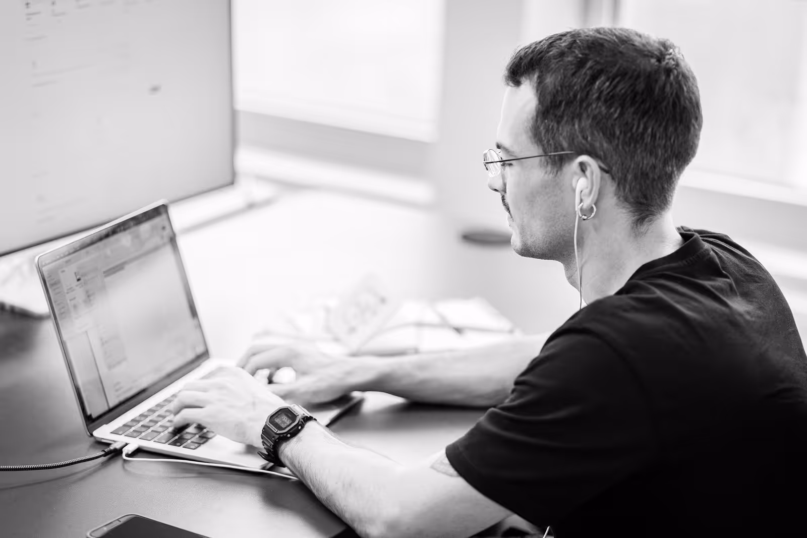 Mitarbeiter mit Brille und Kopfhörern arbeitet konzentriert an einem Laptop in einem modernen Büro.