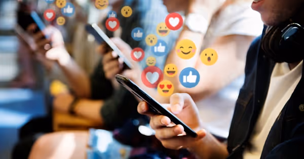 People using smartphones with social media emojis floating around them.