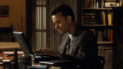 Tom Hanks typing frustratingly on a laptop.