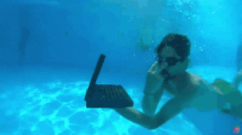 Person using a laptop underwater in a pool.