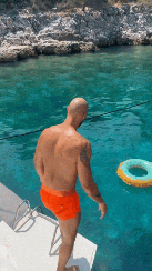 Man dives into clear blue water from a boat, with a turquoise inflatable ring nearby.