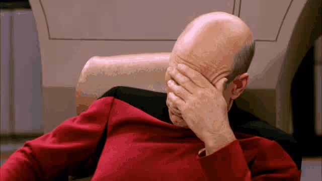 Bald man sitting stressed on a chair with head covered by his hand