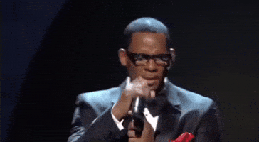 R. Kelly performing on stage, holding a microphone and wearing glasses