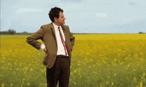 Mr. Bean standing in a field waiting looking at his watch.