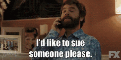 A man with a beard talking on a phone with a serious expression and the caption "I'd like to sue someone please."