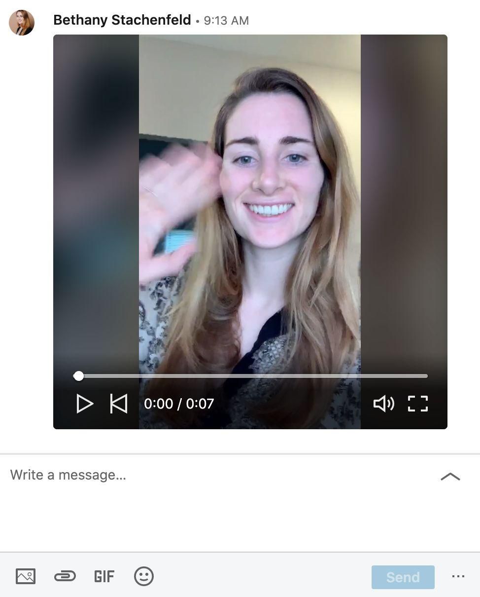 A video still of a smiling woman with long brown hair waving, embedded in a message interface.