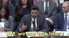 A man in a suit speaking at a formal hearing or panel discussion, seated at a table with microphones, while others sit behind him. Yellow caption text on the image reads, “DM, we can talk later.”
