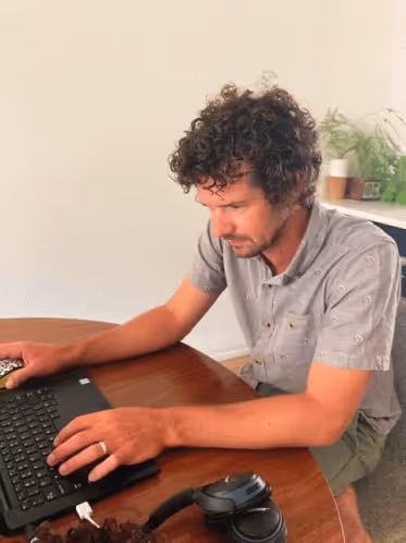 A man working from home on his laptop with headphones around his neck.