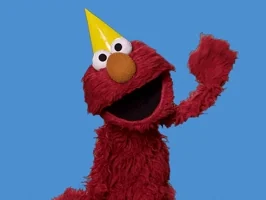 Elmo wearing a party hat waves.
