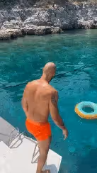 Man dives into clear blue water from a boat, with a turquoise inflatable ring nearby.