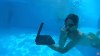 Person using a laptop underwater in a pool.