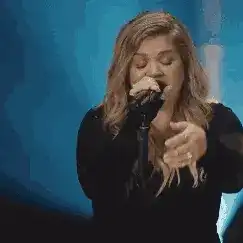 Kelly Clarkson singing into a microphone on stage.