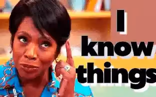 A Black woman with dark curly hair wearing a blue shirt with a gold chain print looks thoughtful and says "I know things" 