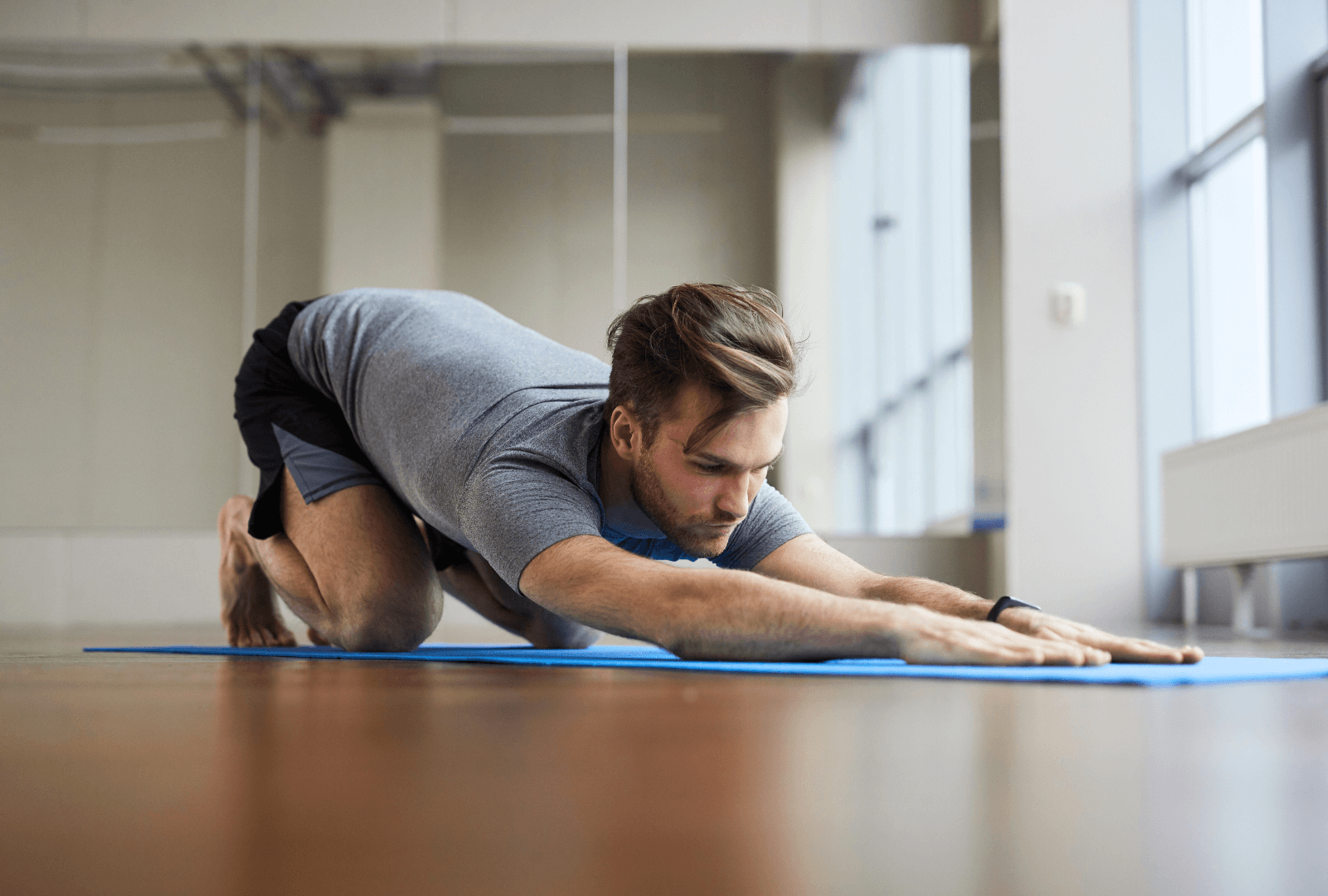A man stretches on his knees performing a restorative yoga pose in a yoga studio.