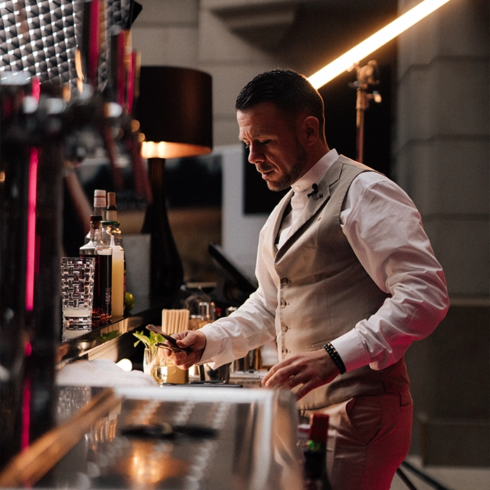 A male bartender making a cocktail dressed in a waistcoat under dark lighting