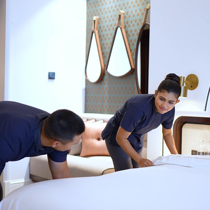 Two Marriott employees smiling at one another and making hotel room bed.