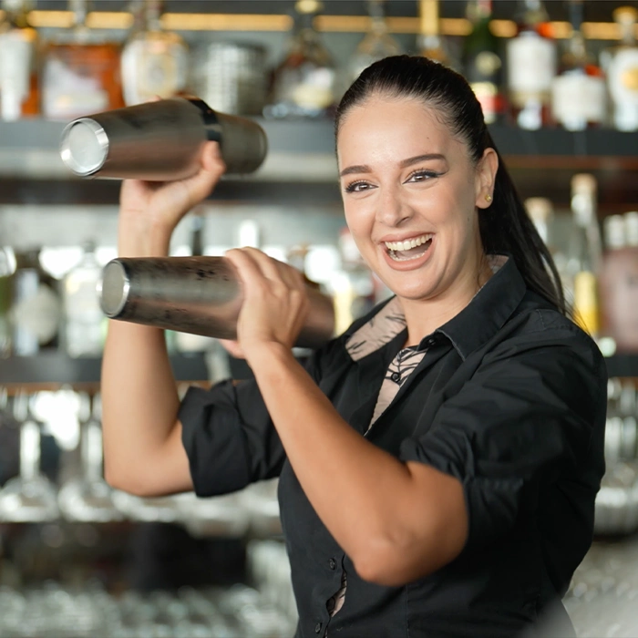 Female bartender smiling whilst making a cocktail.