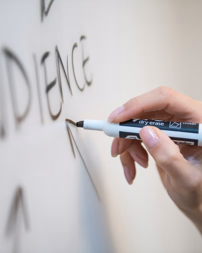 A photo of a person's hand writing on a white board in black marker.