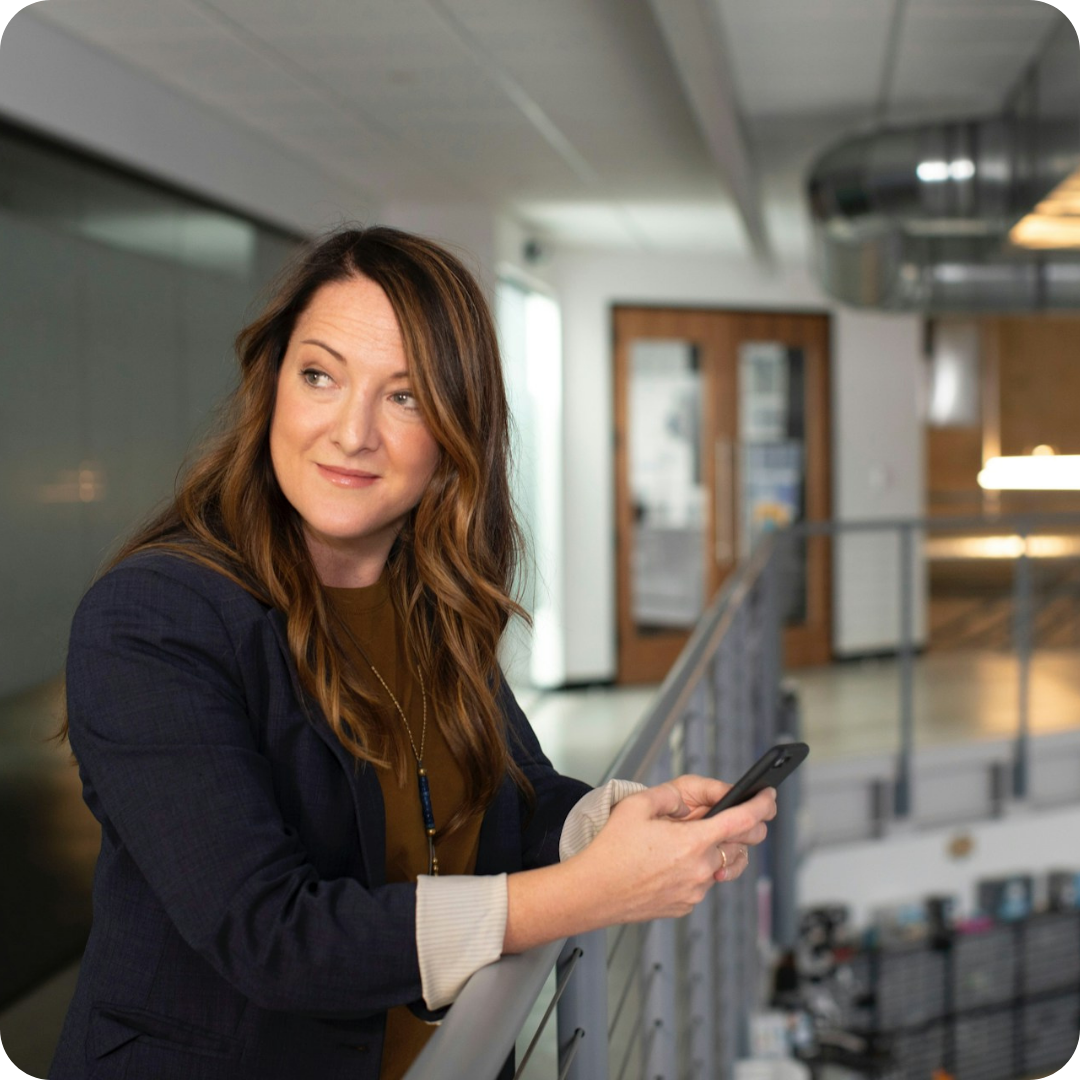 A lady standing, holding her phone, looking like she has a great sense of relief.