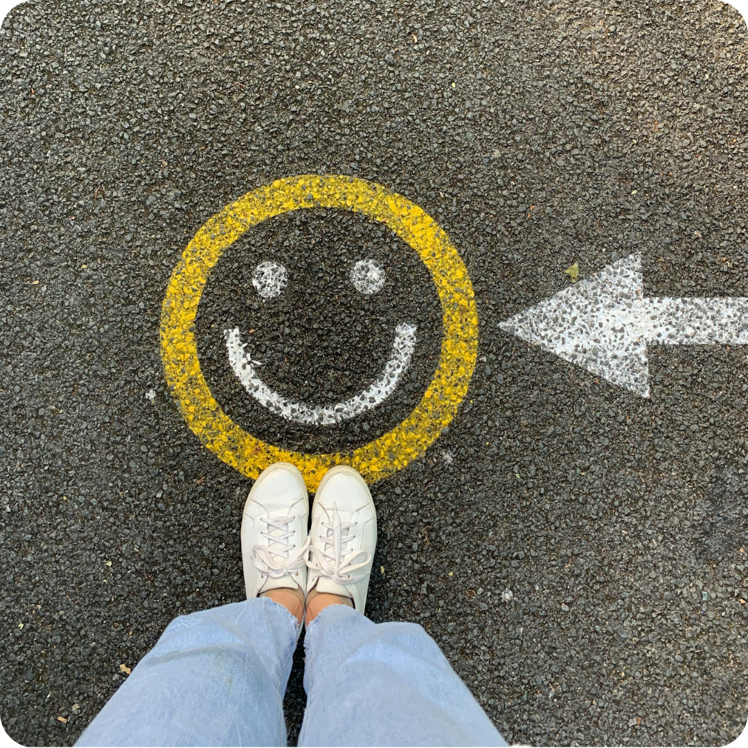 A person stood in front of a yellow smiley face painted on a road with a white arrow pointing towards it.