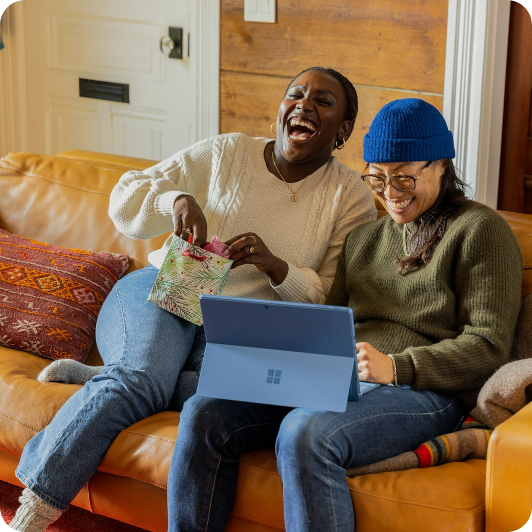 A photo of two colleagues laughing together in front of their computer screen. 