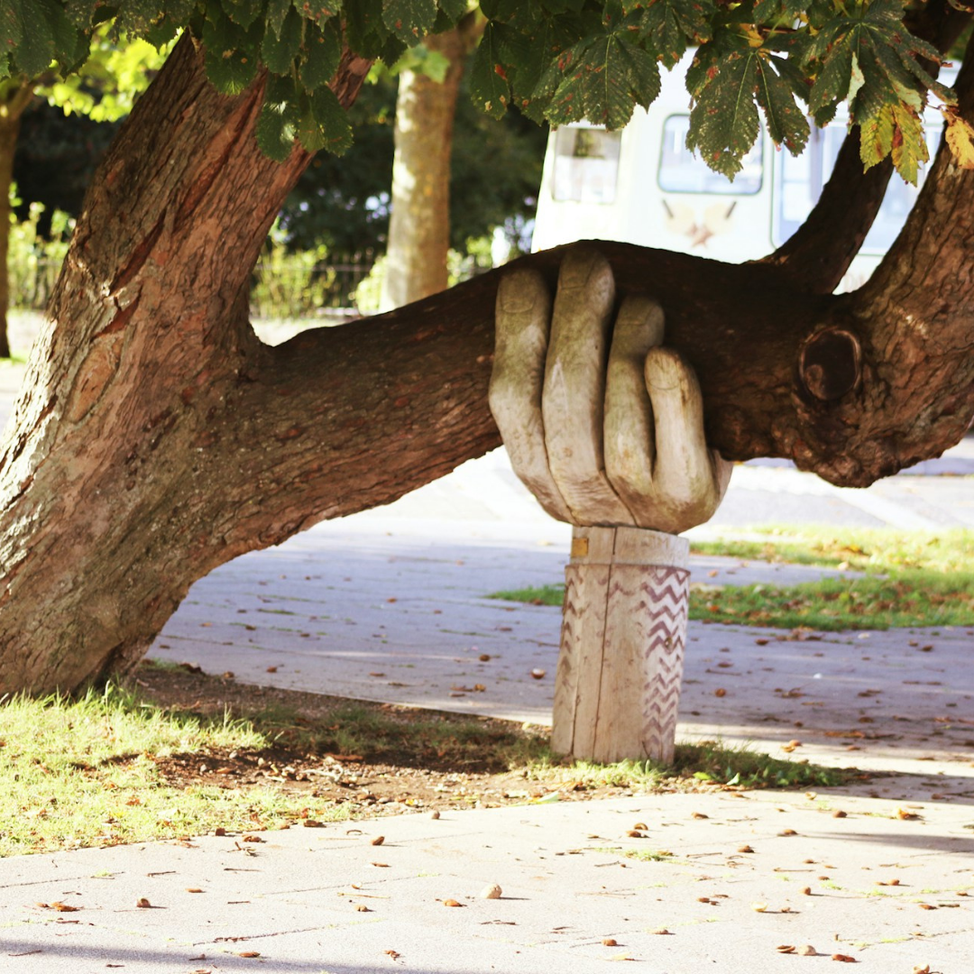 A photo of a wooden statue of a hand holding up a very thick tree branch.t