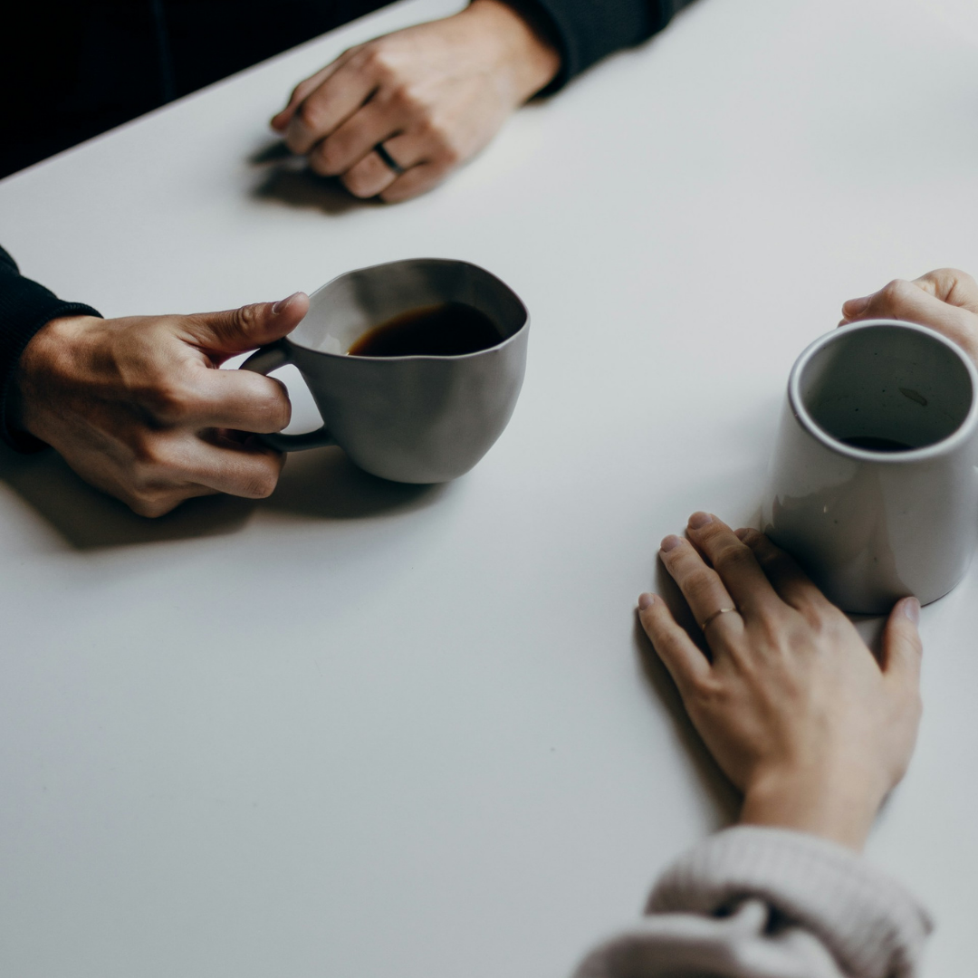 A photo of two colleagues sitting opposite one another holding hot drinks.