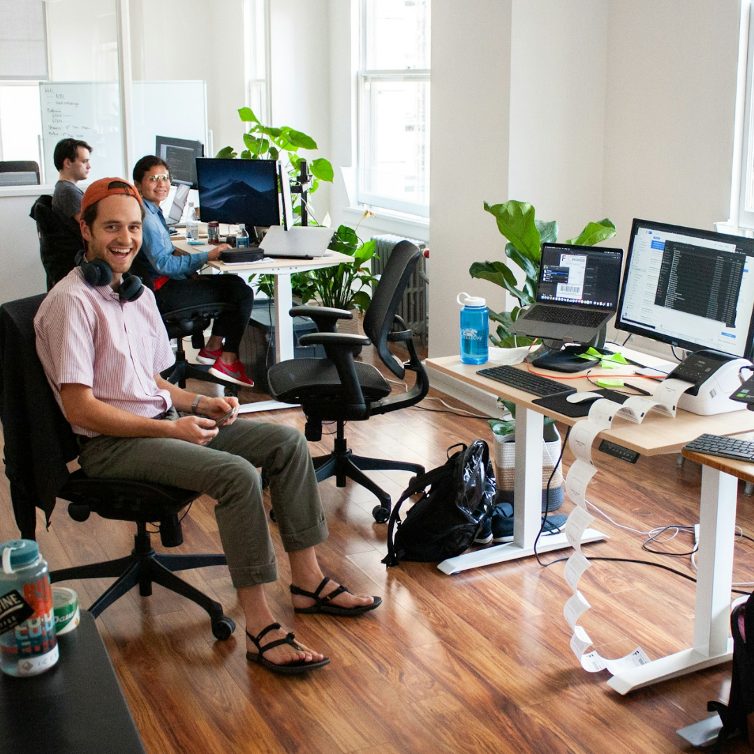 A male employee sat at his desk looking at the camera whilst smiling. 