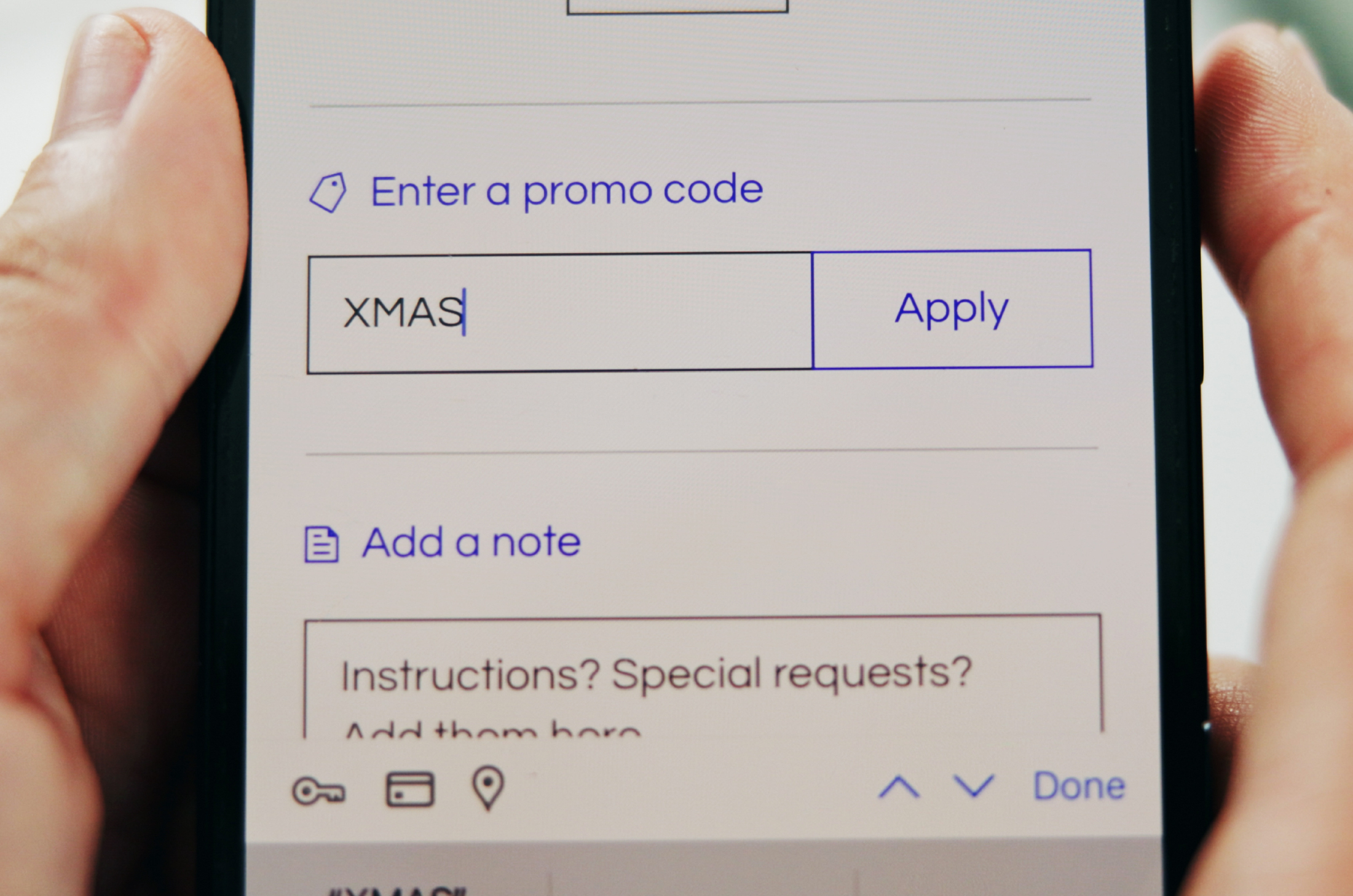 A hand holding a phone that has a promo code entered into a checkout screen.