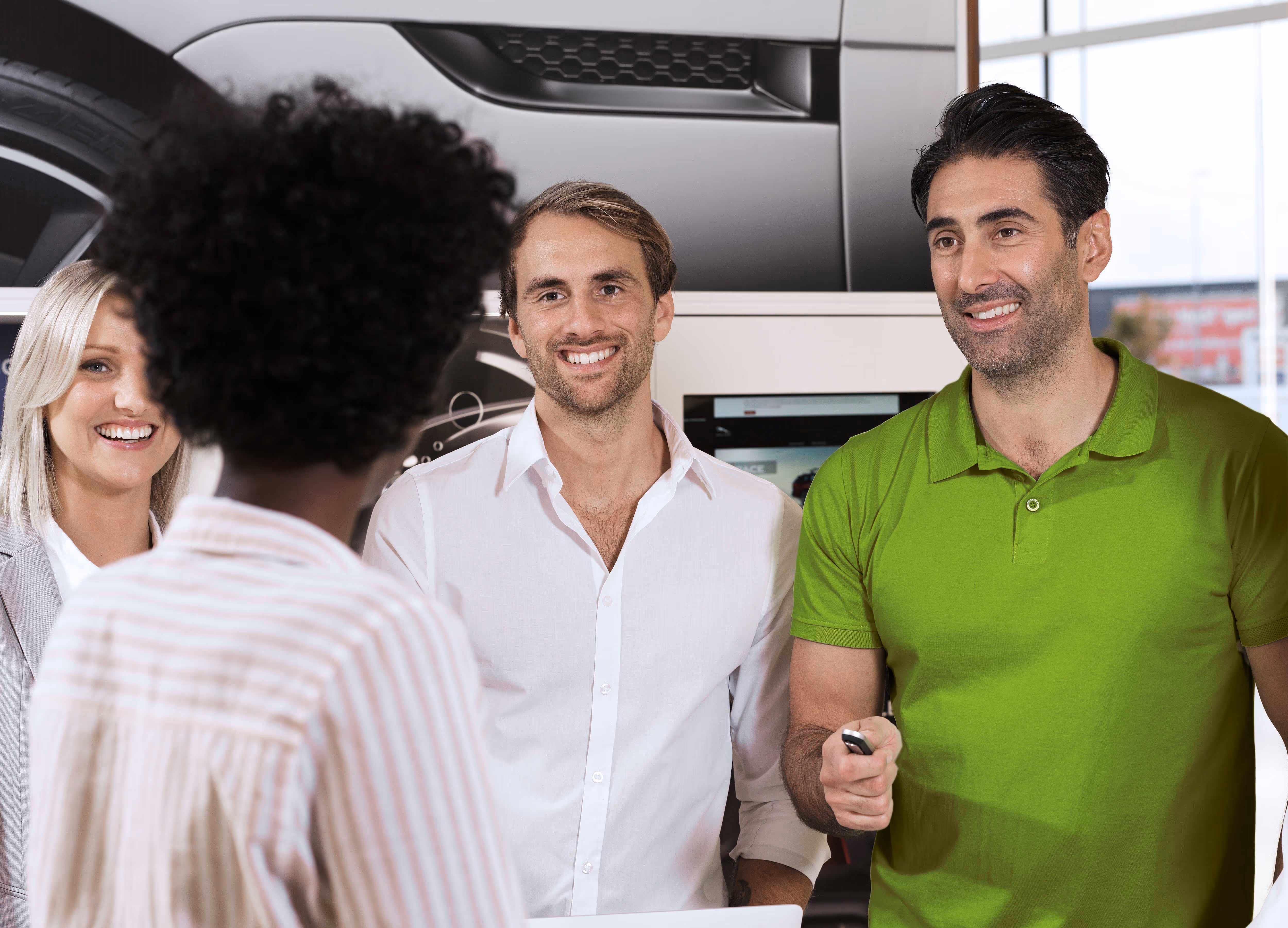 Three people smiling and talking to a person standing in front of them at a car dealership.