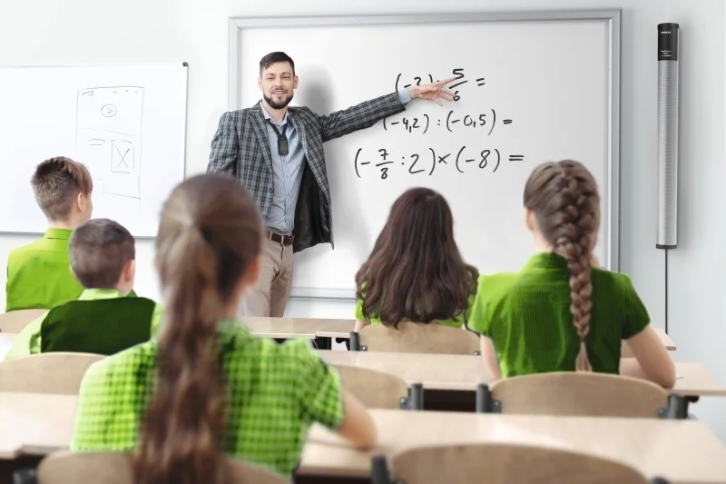 A teacher explains math equations on a whiteboard to a classroom of students.