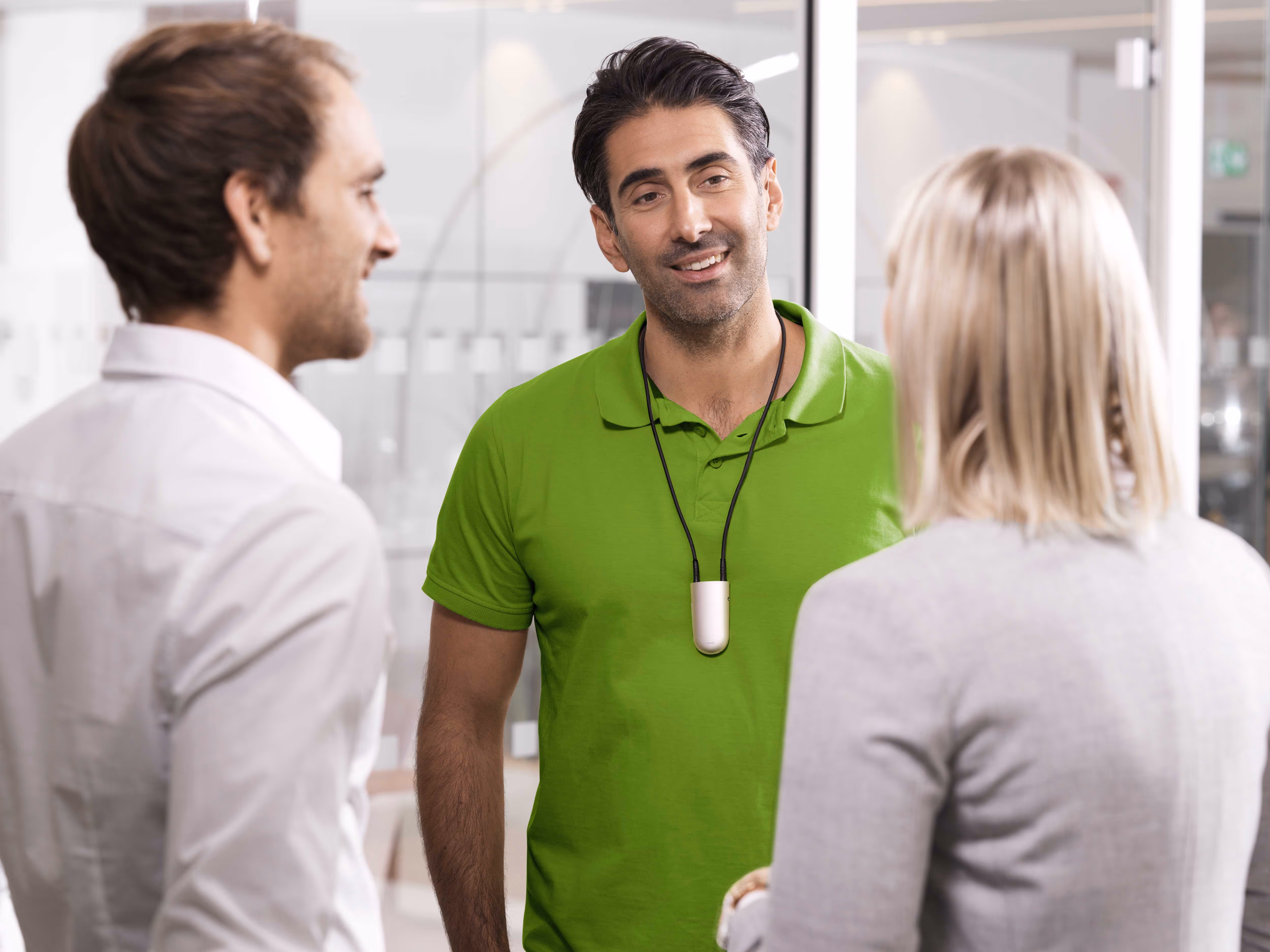 Three people having a friendly conversation, with a man in a green shirt and two others listening.