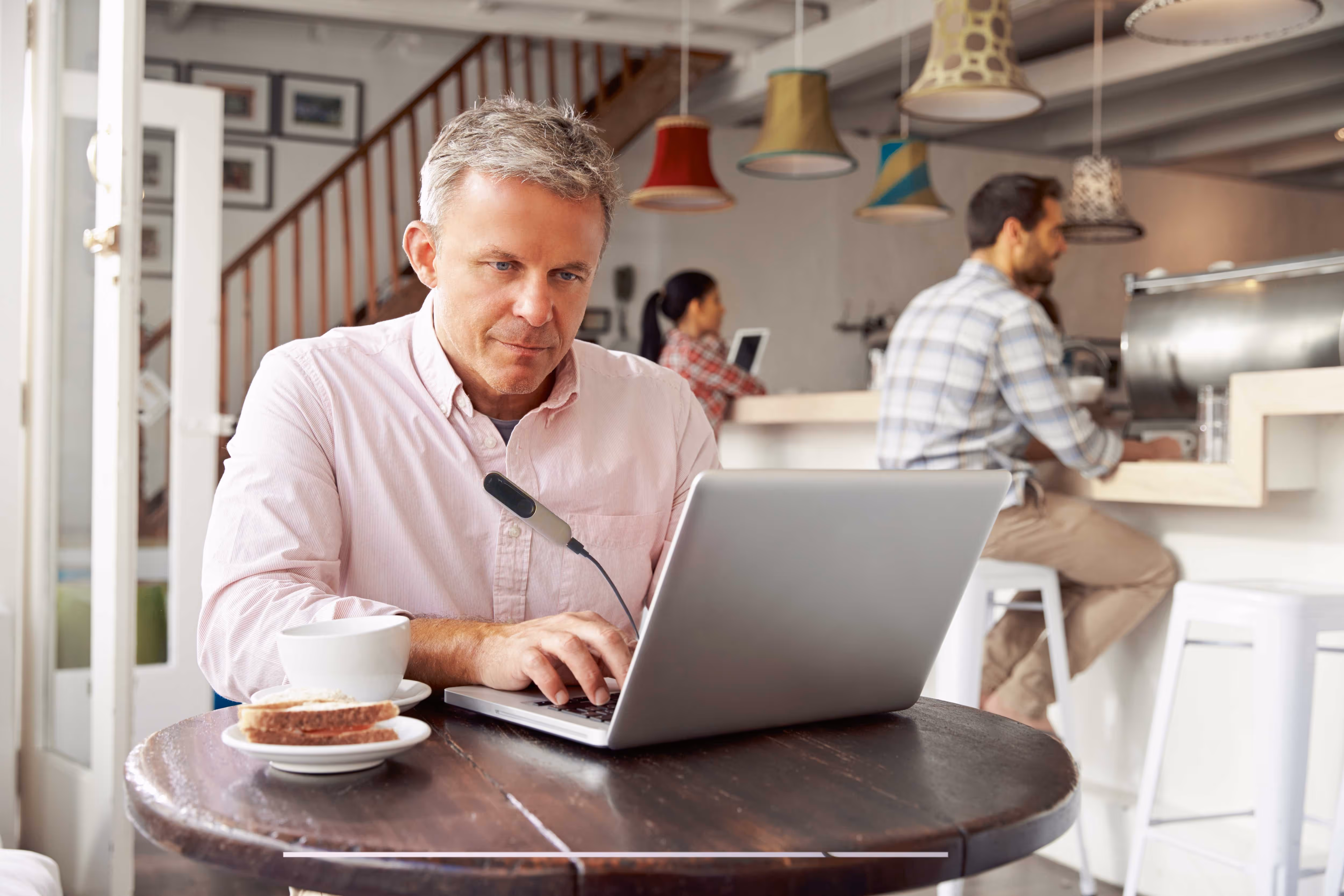 Man working on a laptop at a café table with a coffee and pastry nearby.