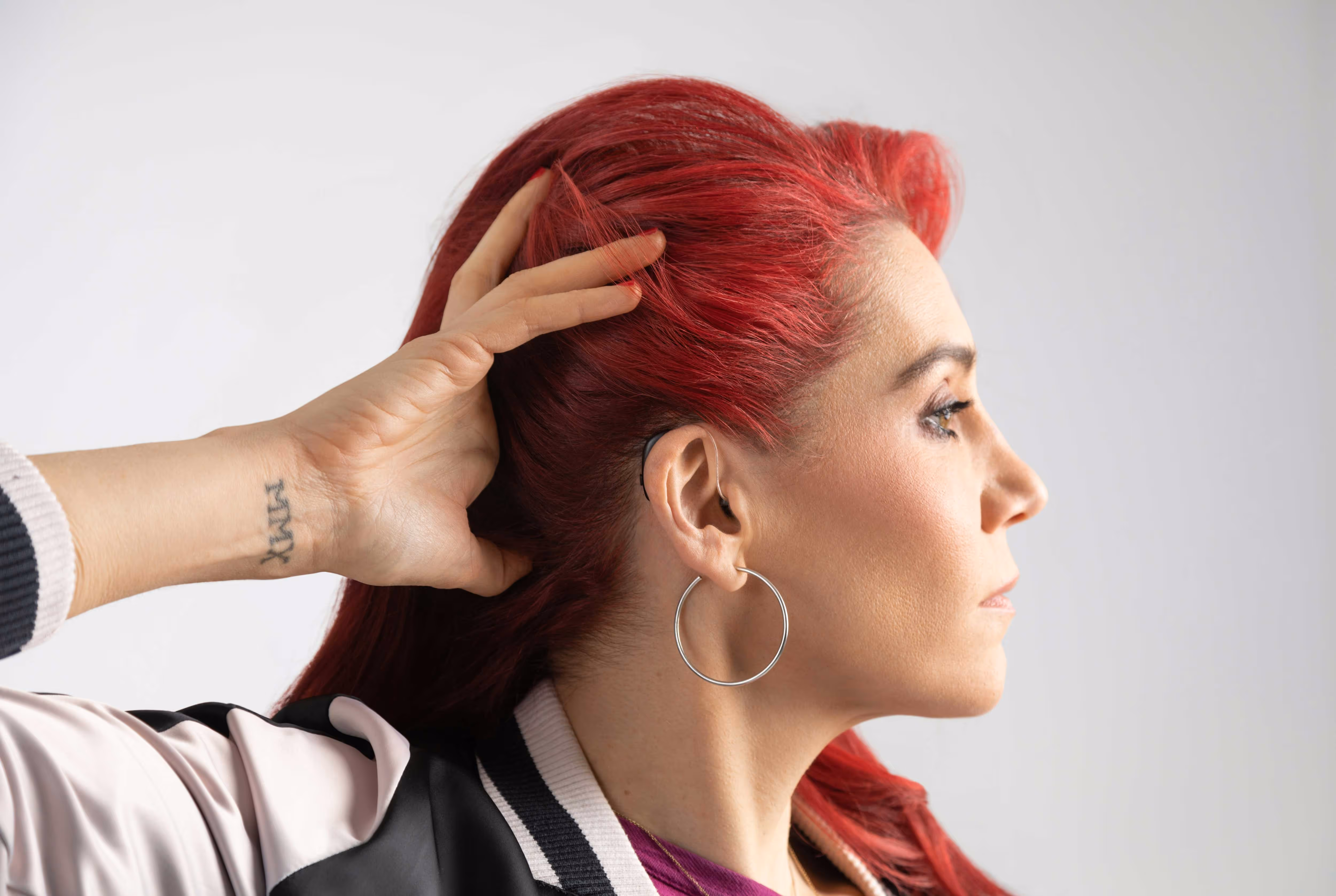 Person with red hair and hoop earrings holds the back of their head, looking to the side.