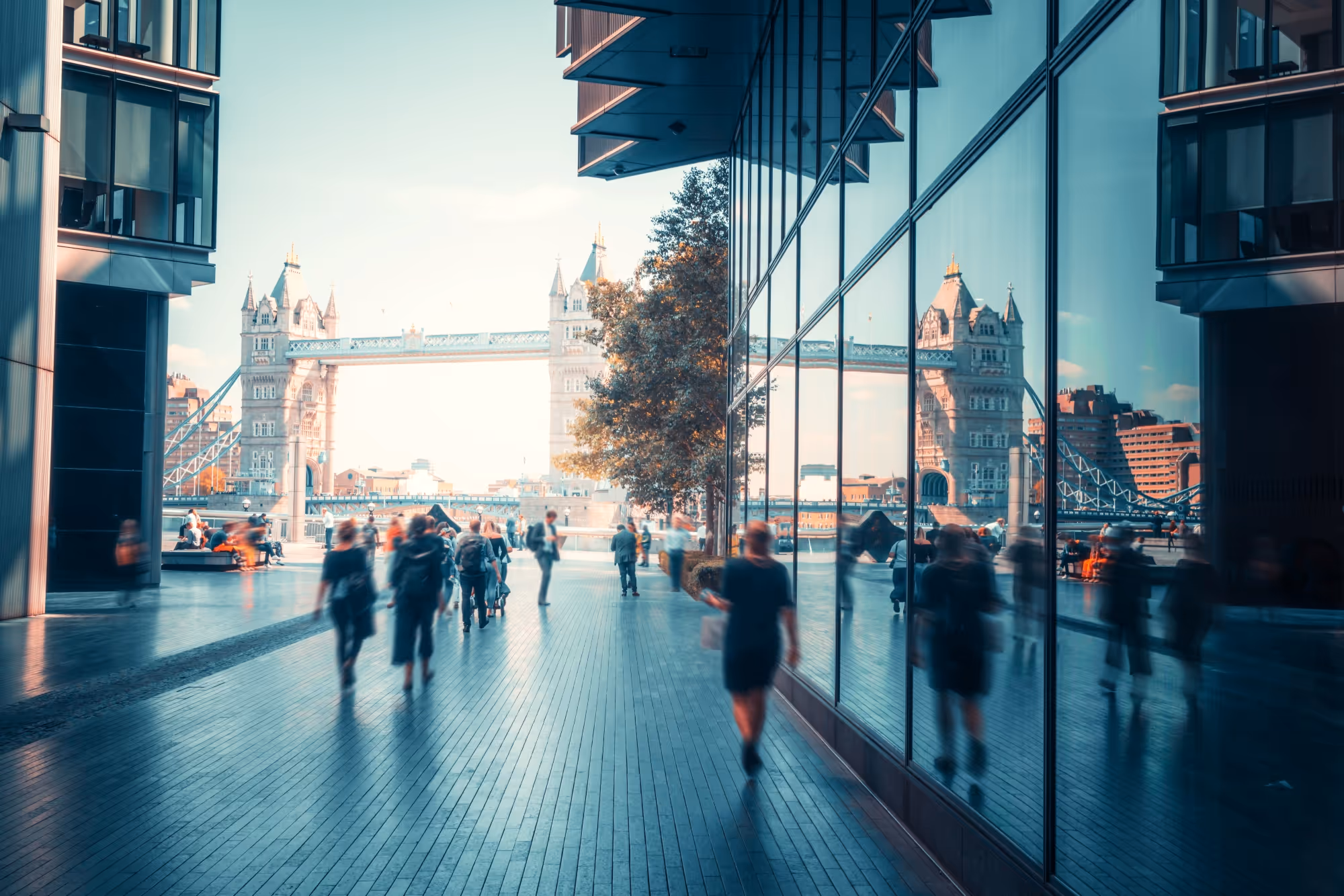 People walking next to the Thames River in London with Tower Bridge in the background