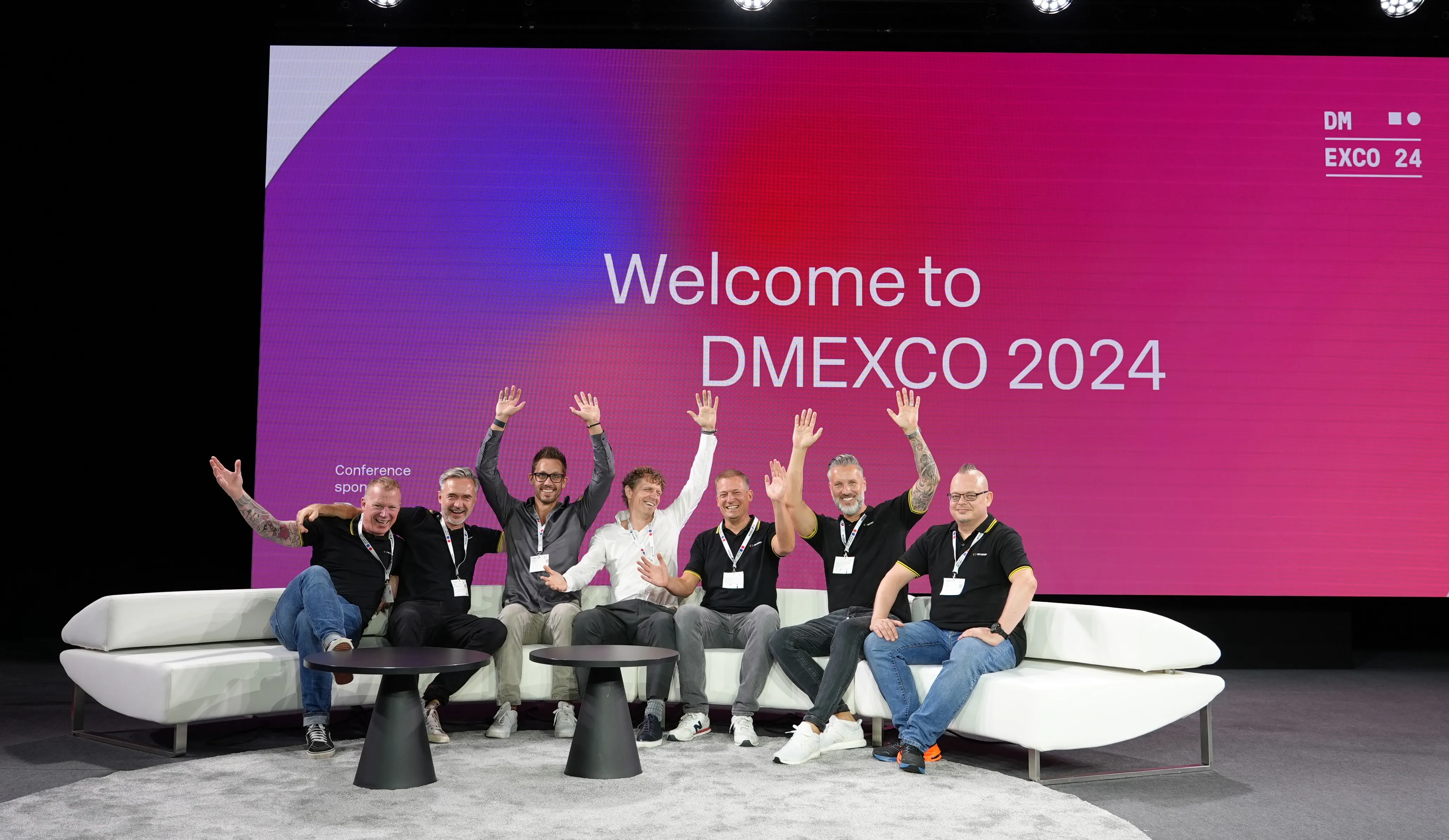 Warum du mit uns auf der DMEXCO sprechen solltest? Wir machen deine digitale Platform zukunftsfähig, umsatzwirksam und sorgen für technische KI-Readyness. Auf dem Bild sieht man Bitgrip-Mitarbeitende auf einer DMEXCO-Bühne sitzend auf einem Sofa.