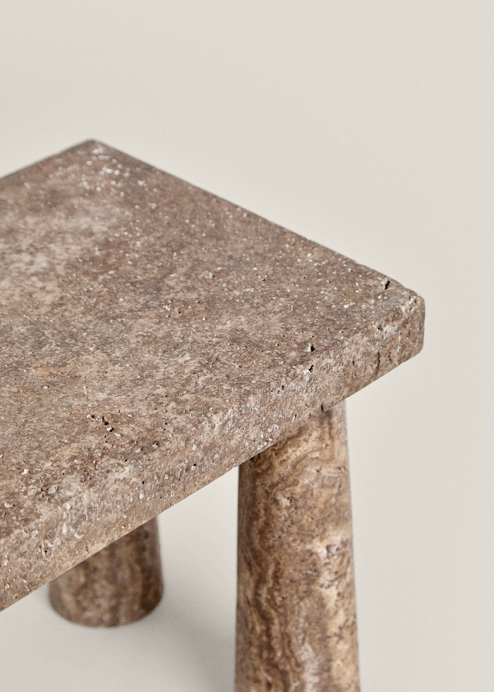 Close-up of the Tap stool's pitted travertine top edge and a veined, banded leg in warm brown tones.