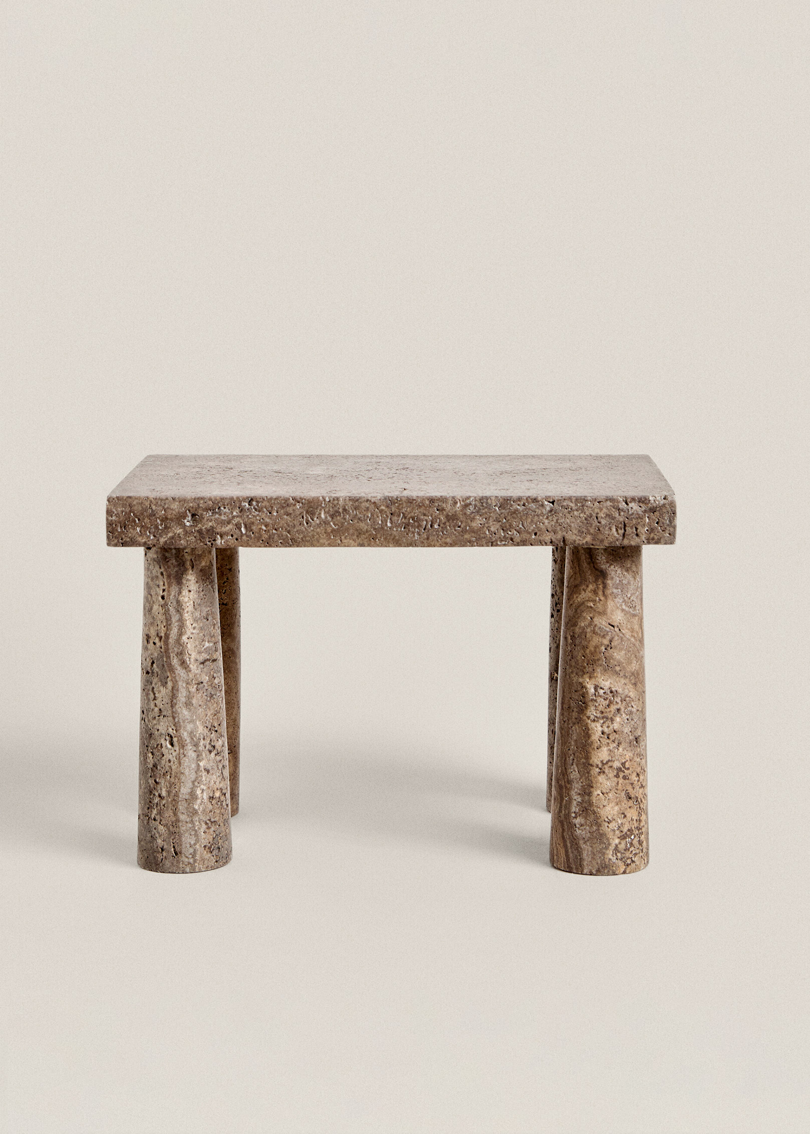 Front view of the Tap stool: a thick rectangular travertine top on four tapered legs, on a plain cream background.