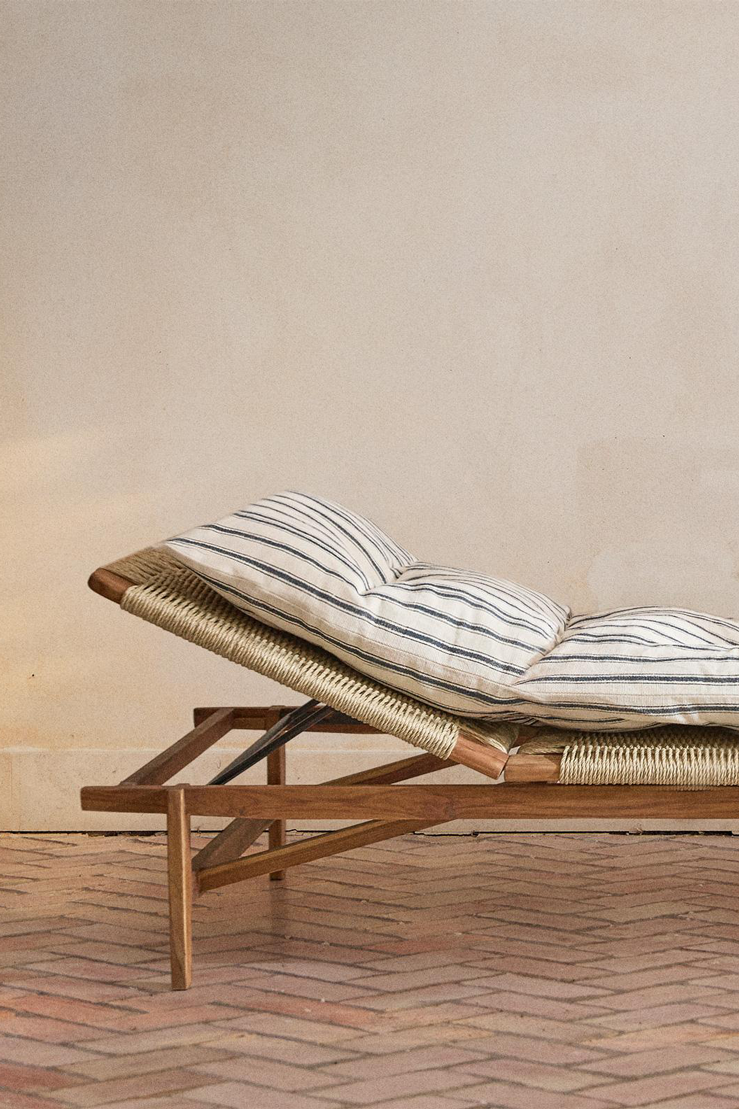 Cord sun lounger in profile with its back raised, a teak frame with woven cord and a thick cream cushion with navy stripes, on a terracotta herringbone floor.